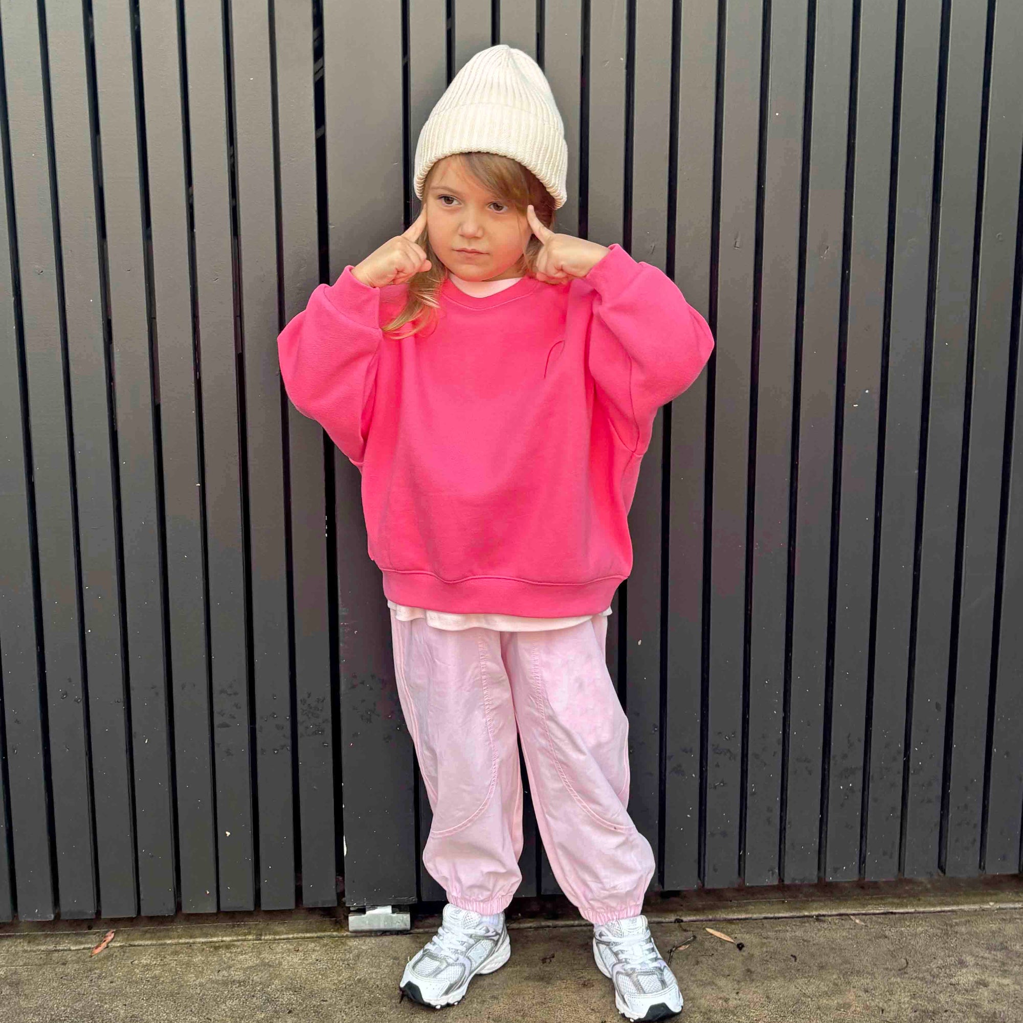 Child wearing a pink outfit with a white beanie against a dark vertical panel background