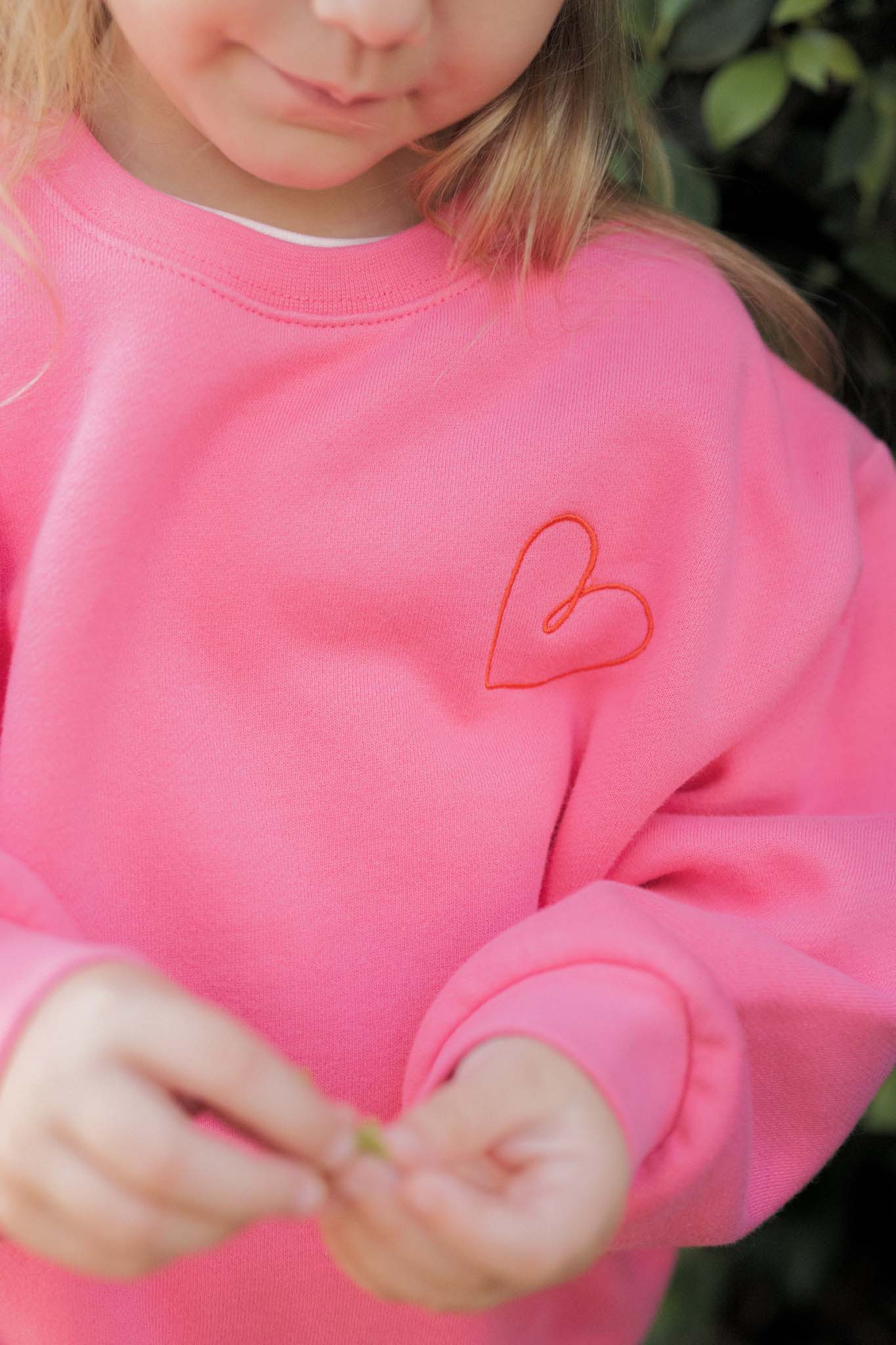 Person wearing a pink sweatshirt with a heart design outdoors