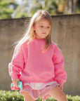 A girl in a pink sweatshirt and shorts.
