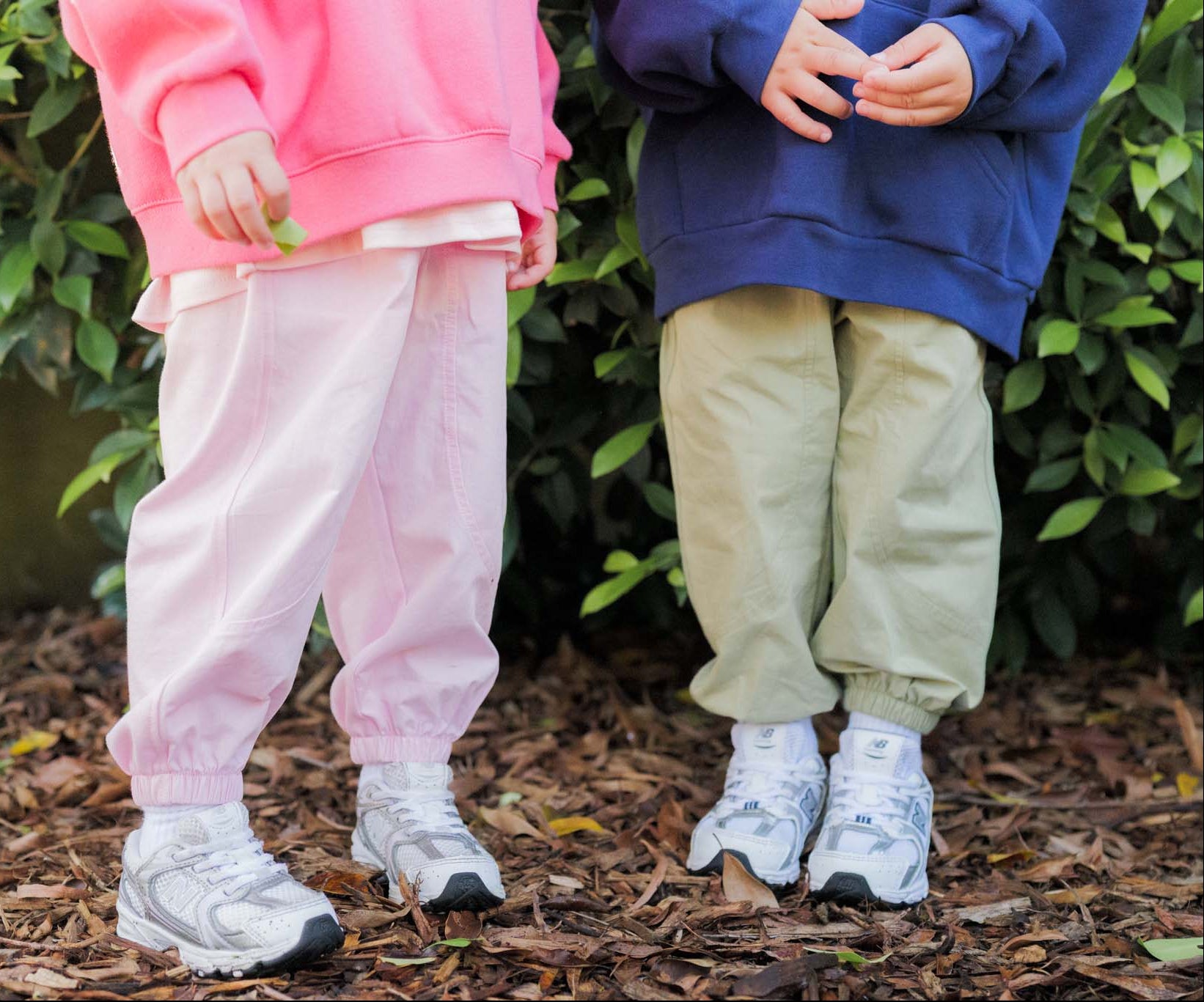 Two children standing outdoors, wearing colorful outfits and white sneakers.