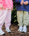 Two children standing outdoors, wearing colorful outfits and white sneakers.