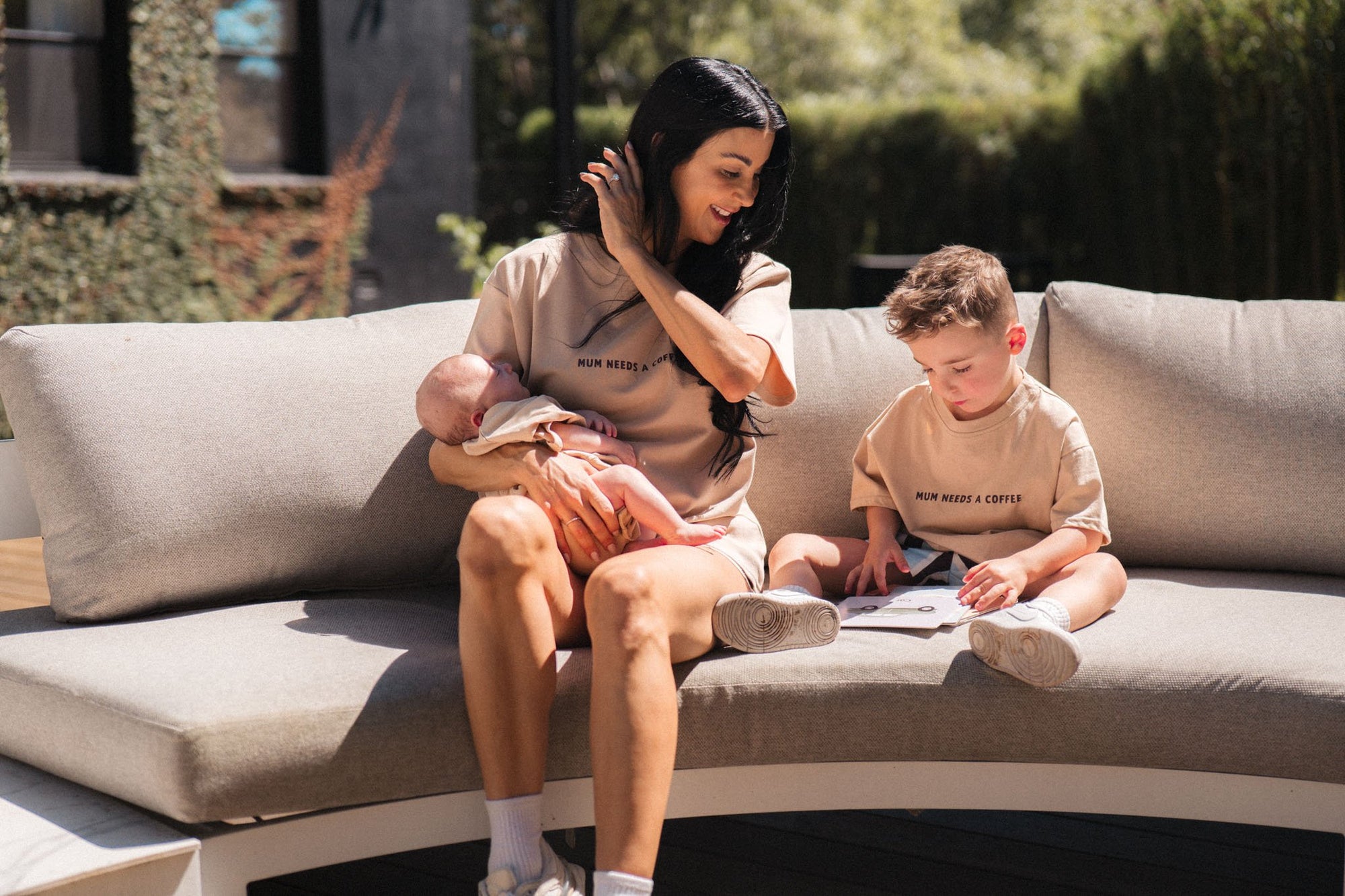 Woman holding a baby and interacting with a child on a outdoor sofa