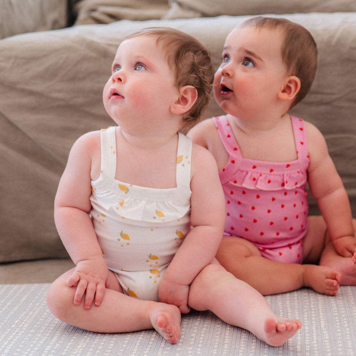Three babies sitting on a couch wearing matching outfits.