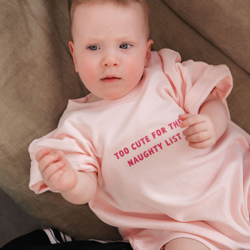 Baby wearing a pink sweatshirt with text sitting on a couch.