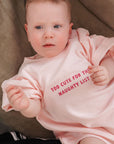 Baby wearing a pink sweatshirt with text sitting on a couch.